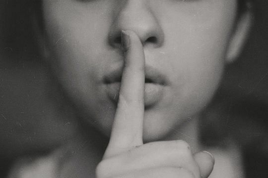 Person mit erhobenem Zeigefinger vor den Lippen in schwarz-weiß
