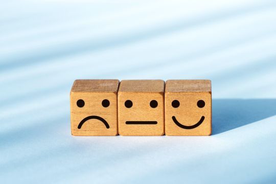 Drei Holzwürfel mit Gesichtern von unzufrieden bis zufrieden
