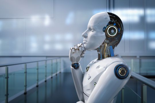 Ein humanoider Roboter mit einem weißen, futuristischen Design steht in einem modernen, lichtdurchfluteten Raum. Der Roboter hat eine nachdenkliche Pose, mit einer Hand am Kinn, als würde er überlegen.