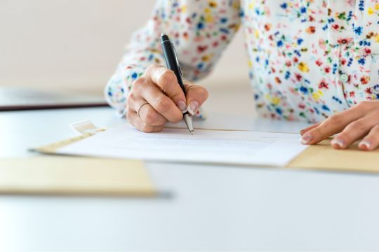 Person sitzt am Tisch und schreibt auf einem Papier