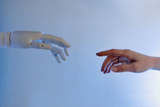 Menschliche Hand und Roboterhand zeigen aufeinander
