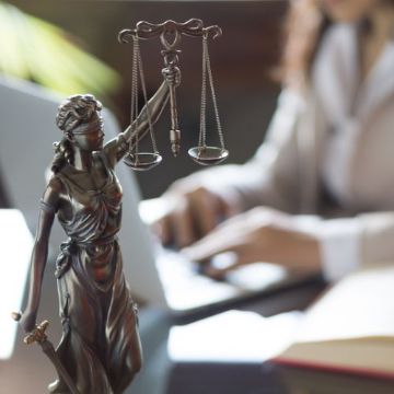 Justitia vor einer Person, die am Laptop arbeitet